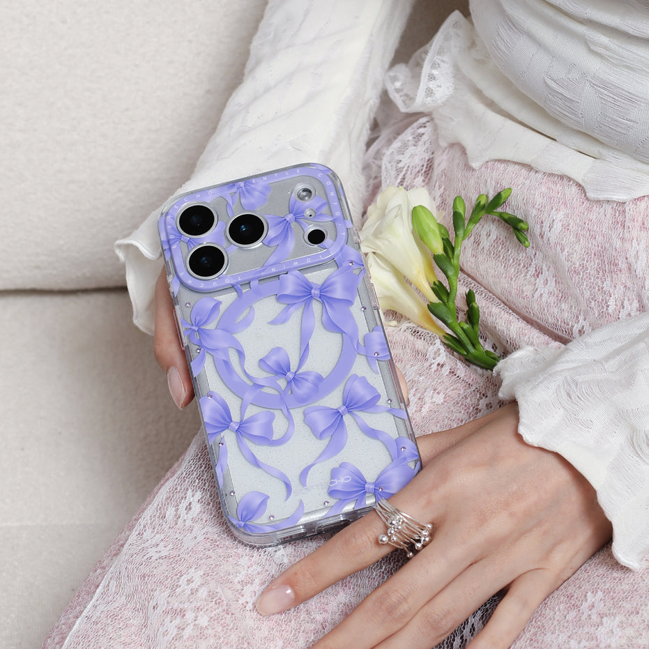Phone case with purple floral design held by a hand, with a white rose on a light pink fabric background.