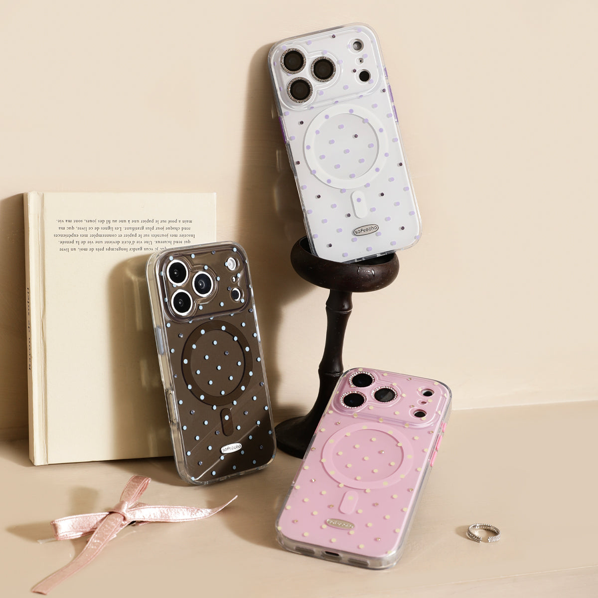 Three phone cases with polka dot designs on a beige surface with a book and ribbon.