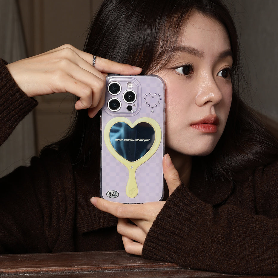 Person holding a phone with a purple case featuring a heart mirror design.