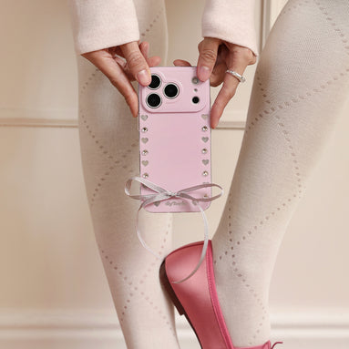 Blush pink MagSafe iPhone case with crystal studs, silver heart accents, and satin bow